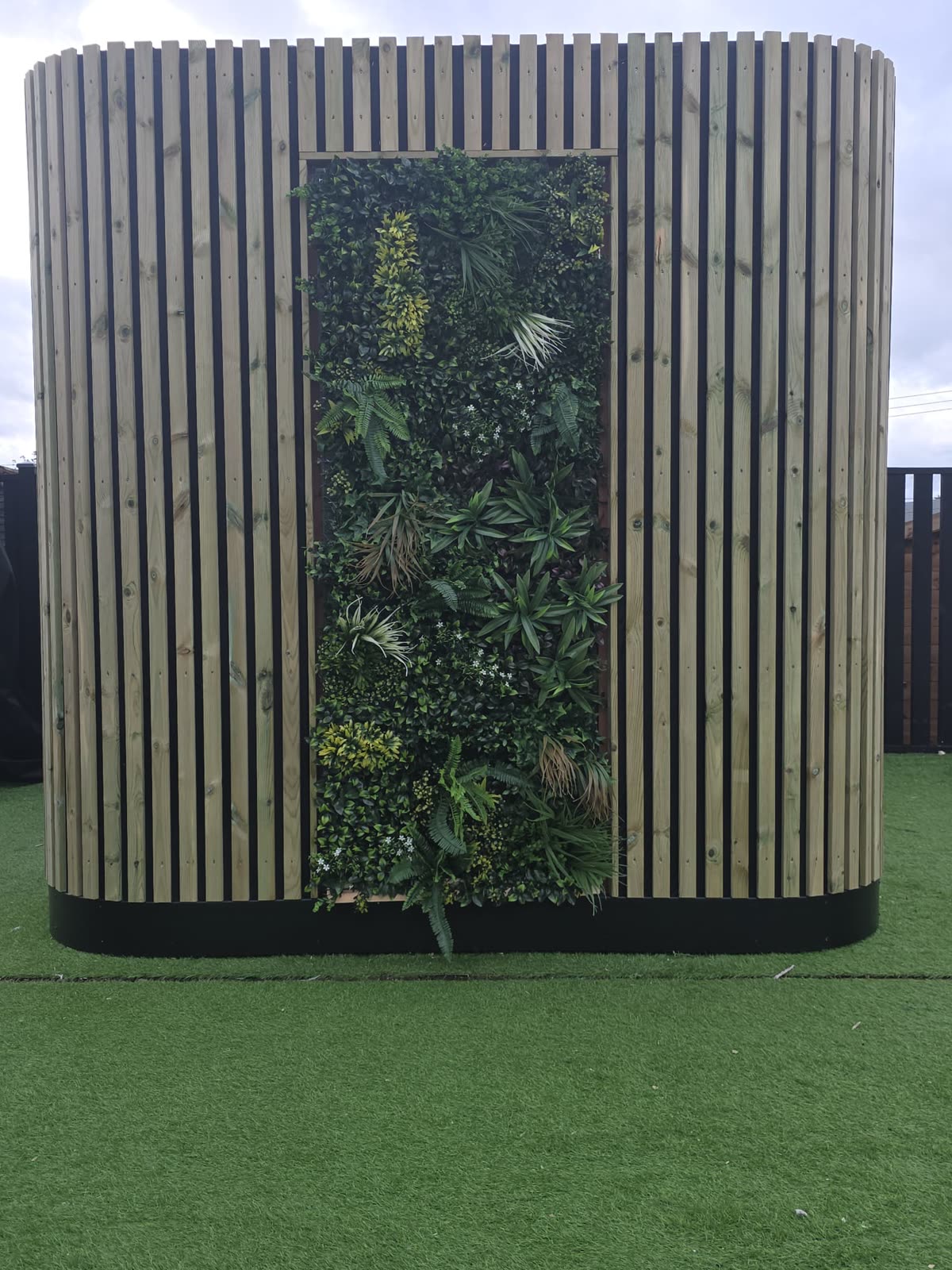 Real-life bespoke POD with rounded timber slatted cladding and a living green plant wall, front view