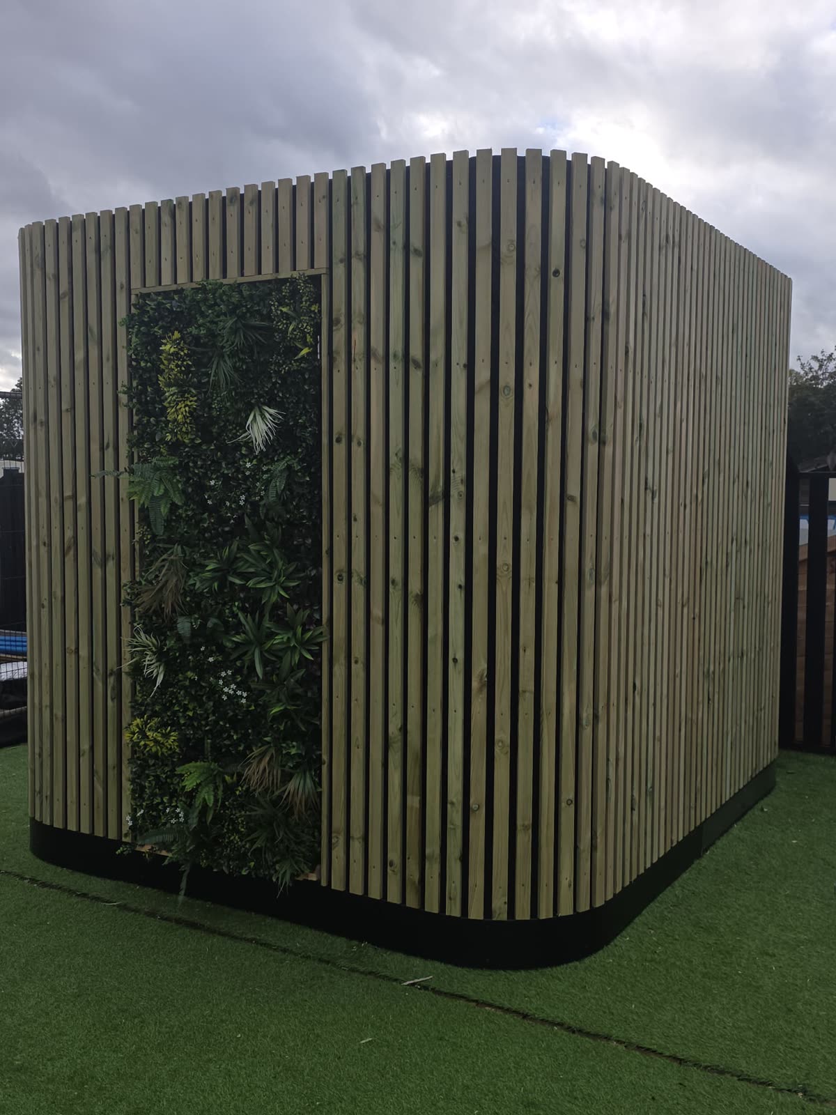 Real-life bespoke POD with rounded corners, timber slats and green wall, three-quarter view